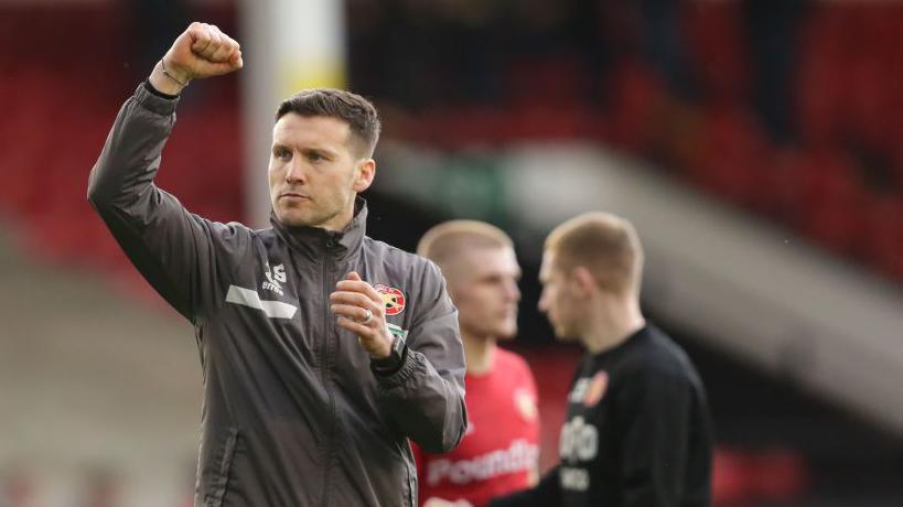 Walsall boss Mat Sadler holds his right fist up to salute the fans after a game