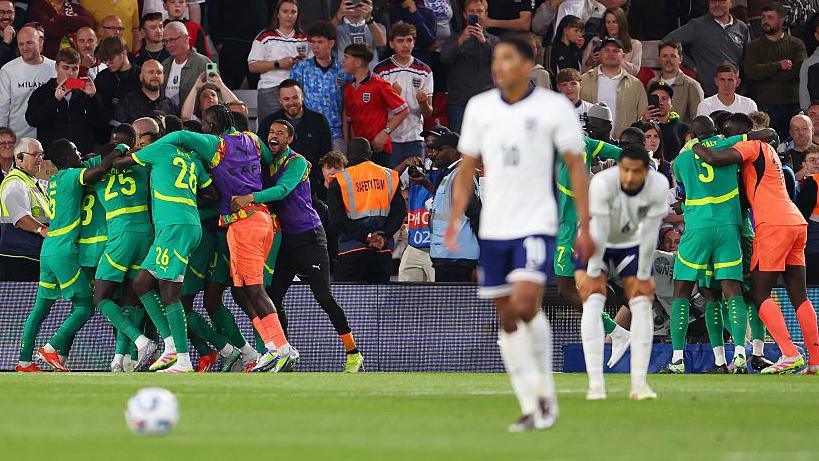 England players in the foreground as Senegal's team celebrate at the side of the pitch