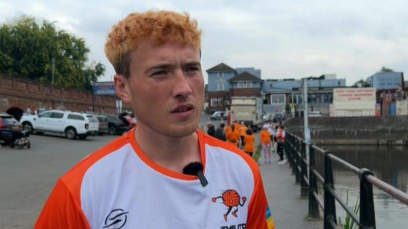 Jordan Adams, standing in a car park wearing a white and orange T-shirt and being interviewed