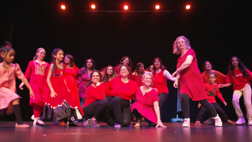 Adult and child dancers on a stage in red costumes.