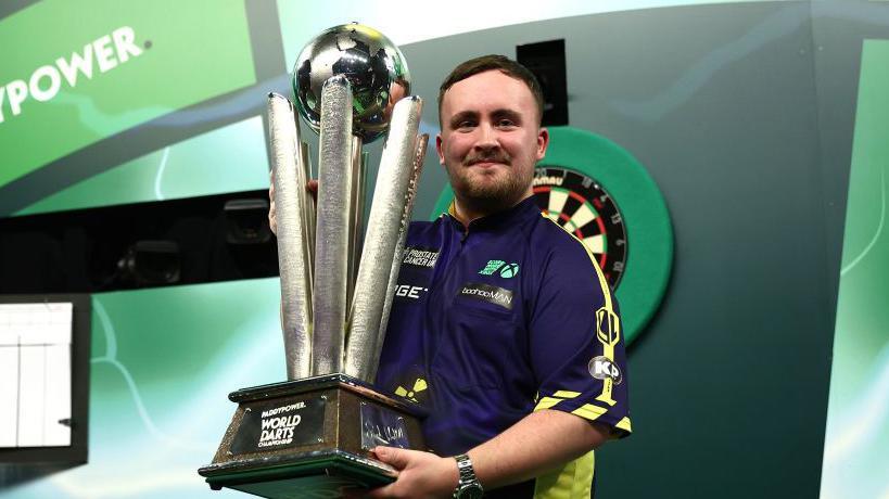 Luke Littler holding the world darts trophy