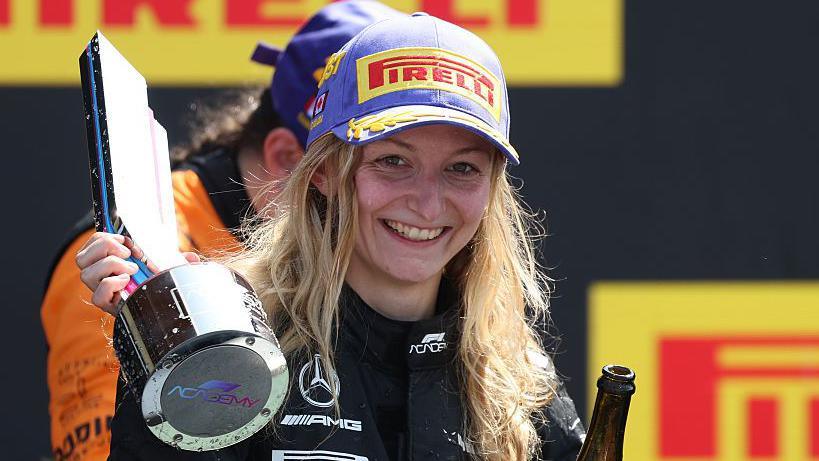 Doriane Pin holding up her trophy on the podium after winning the first F1 Academy race at the Canadian Grand Prix