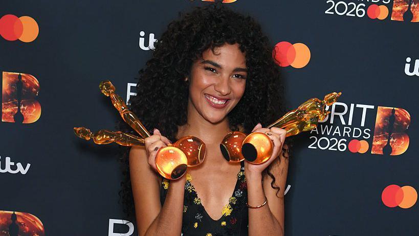Singer Olivia Dean holding four Brit awards