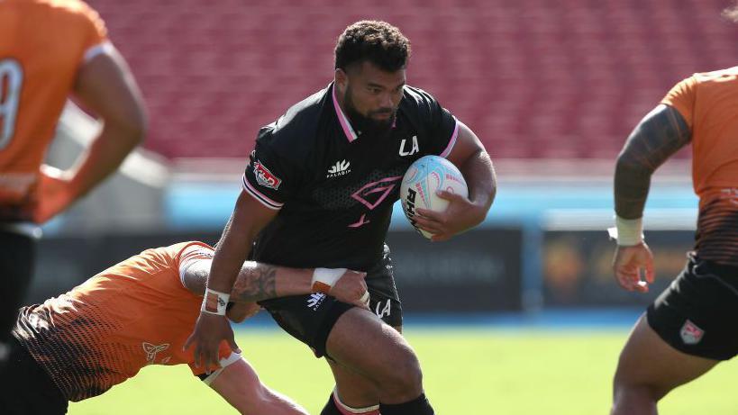 Marco Fepulea'i running with the ball under his left arm while a player tackles him around his waist during a game for LA Giltinis in 2022