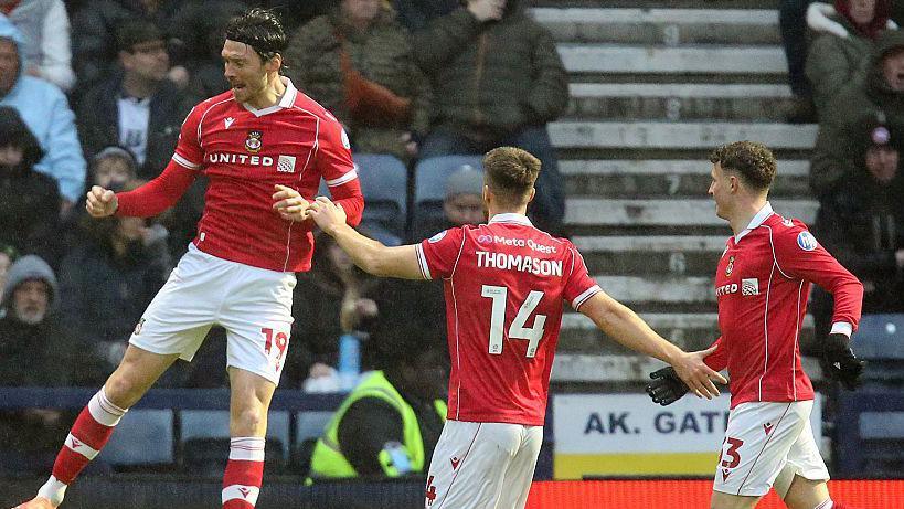Wrexham striker Kieffer Moore (left) celebrates with George Thomason (centre) and Nathan Broadhead (right)