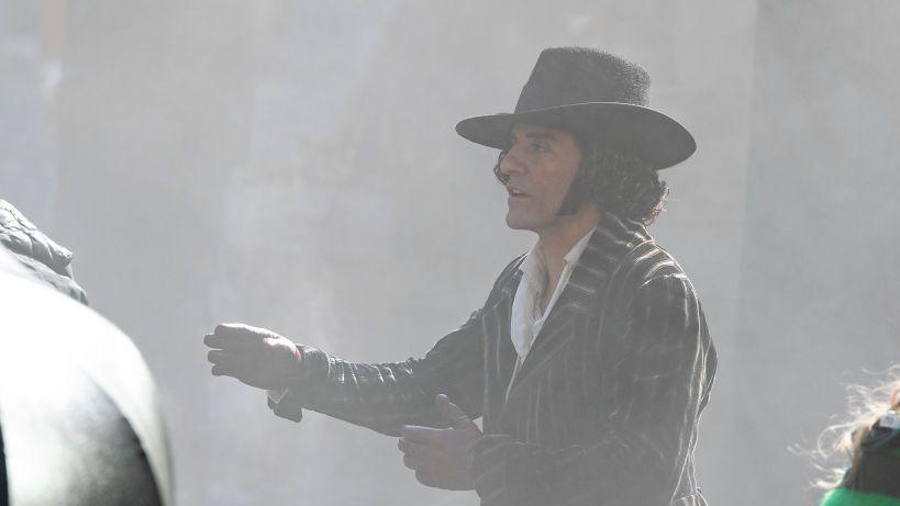 Actor Oscar Isaac wearing a pinstriped suit, wide brimmed hat and leather gloves on set in Edinburgh. He has dark hair.