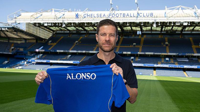 Xabi Alonso holding a Chelsea shirt while posing for a photo at Stamford Bridge