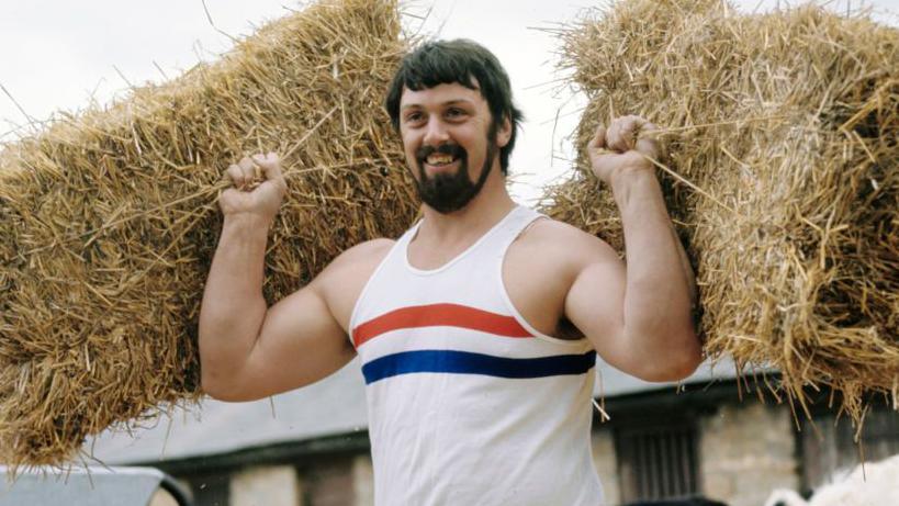 Geoff Capes lifts bales of hay