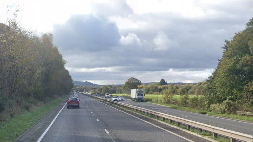 Google image of A38 near Chudleigh Knighton in Devon. Vehicles are travelling on either side of the road. Trees and fields line either side of the carriageway.