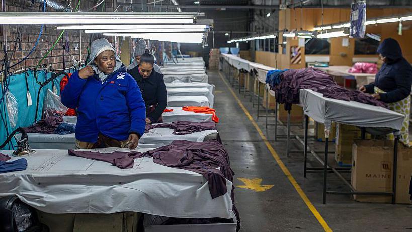 Factory workers, wearing woolly hats and jackets, work on purple-coloured apparel at a factory in Maseru, Lesotho