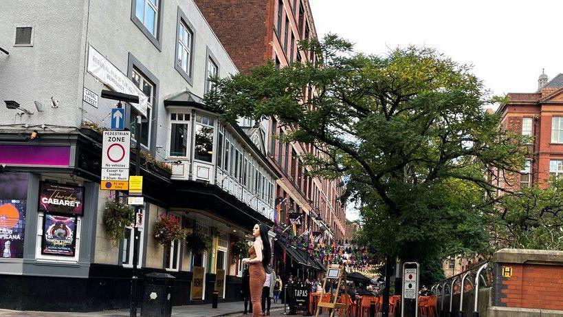 Canal Street with bar furniture on the street across from a bar and a tree in the foreground