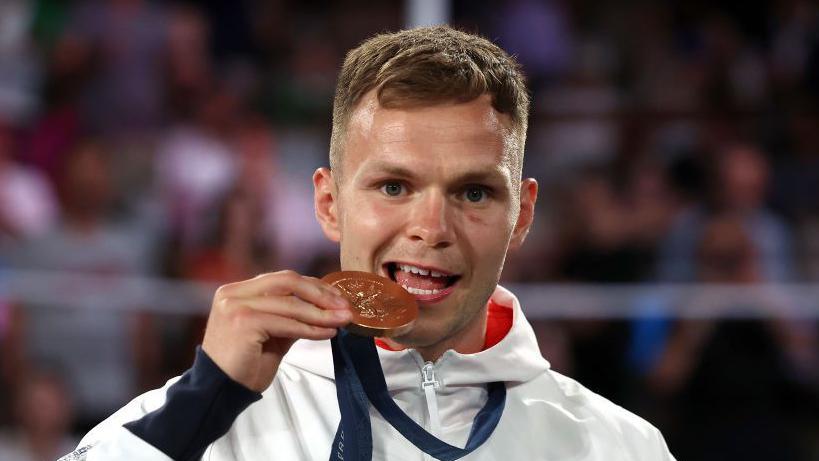 Lewis Richardson bites into his bronze medal