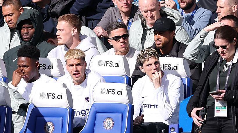 Enzo Fernandez sits behind Chelsea's bench in his normal clothes during defeat to Manchester City