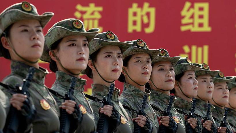 Female soldiers standing in formation holding guns with Chinese writing in background