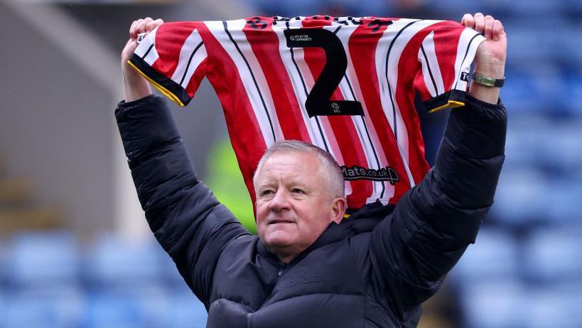 Chris Wilder holds aloft the number two shirt worn by former Sheffield United defender George Baldock, who died in October 