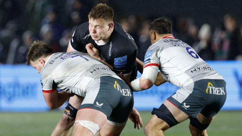 Newcastle's Freddie Lockwood being tackled by two Saracens players