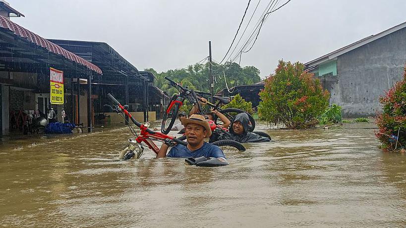 Two people carry bicycles while submerged up to their shoulders in brown water