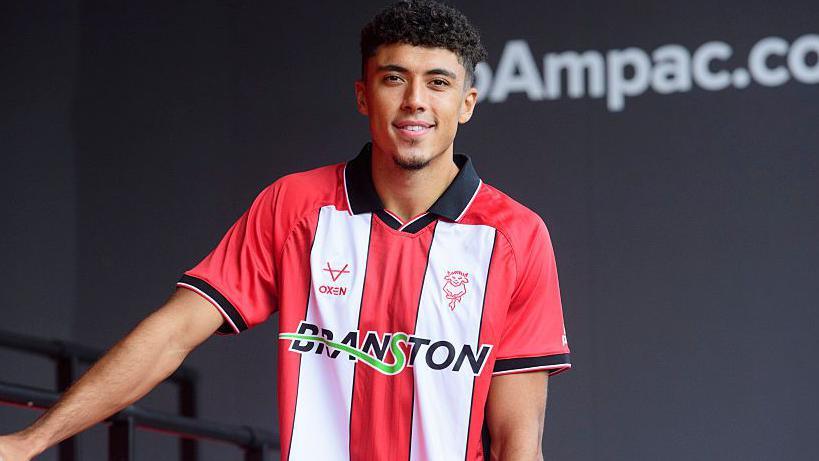 Ethan Wheatley in a red and white-striped Lincoln City shirt after his loan deal was completed