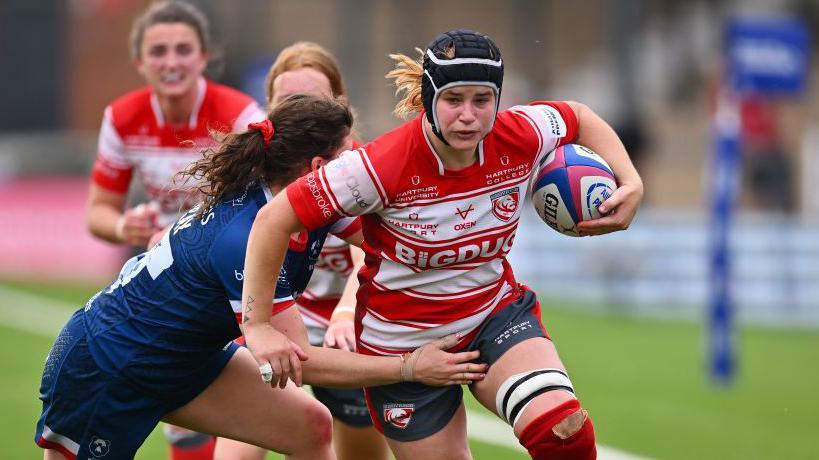Bethan Lewis wears a black headguard and a red and white striped jersey