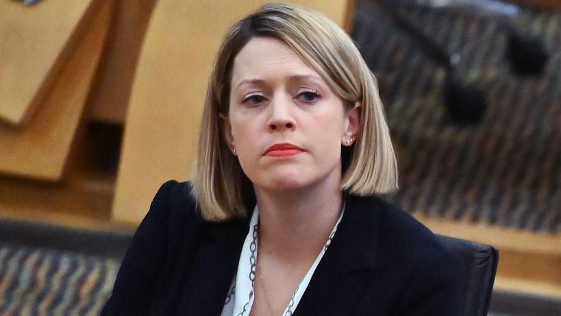 Education Secretary Jenny Gilruth, who has a blonde bob, red lipstick and a black blazer, sitting in the Holyrood chamber