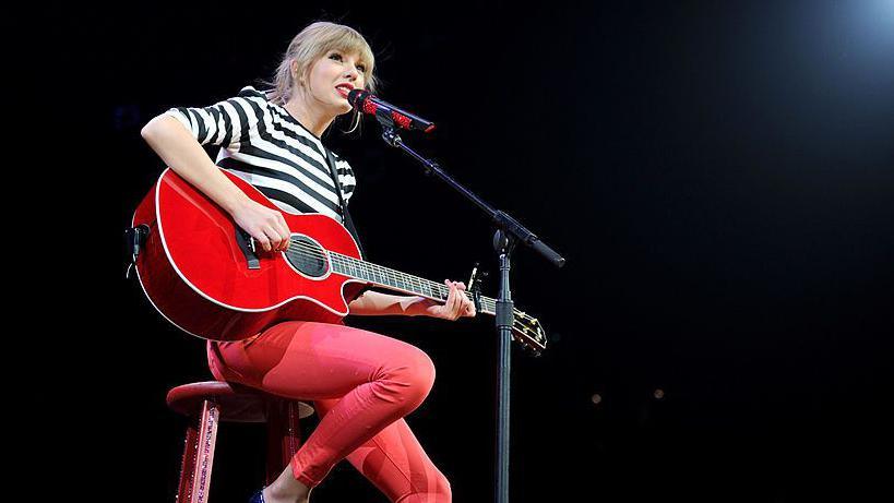 Taylor Swift strums a red guitar during a concert on her Eras Tour