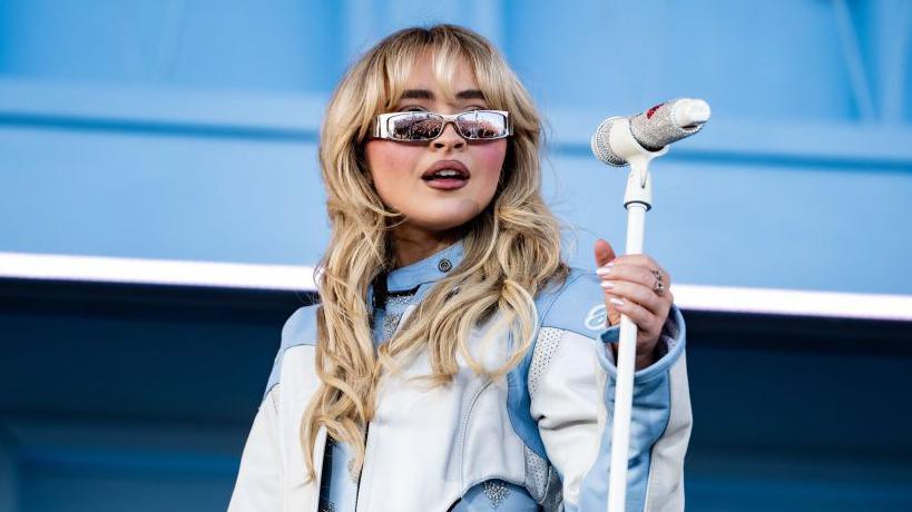 Sabrina Carpenter standing with microphone. 