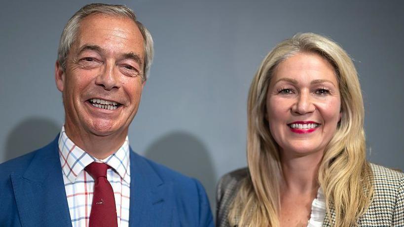 Nigel Farage stood in to the left with Laura Anne Jones to the righjtj, in front of a grey background