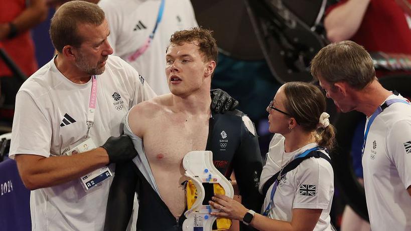 Jack Carlin of Team Great Britain is helped by coaching staff after he crashes in the Keirin final on day sixteen of the Olympic Games Paris 2024 at Saint-Quentin-en-Yvelines Velodrome 