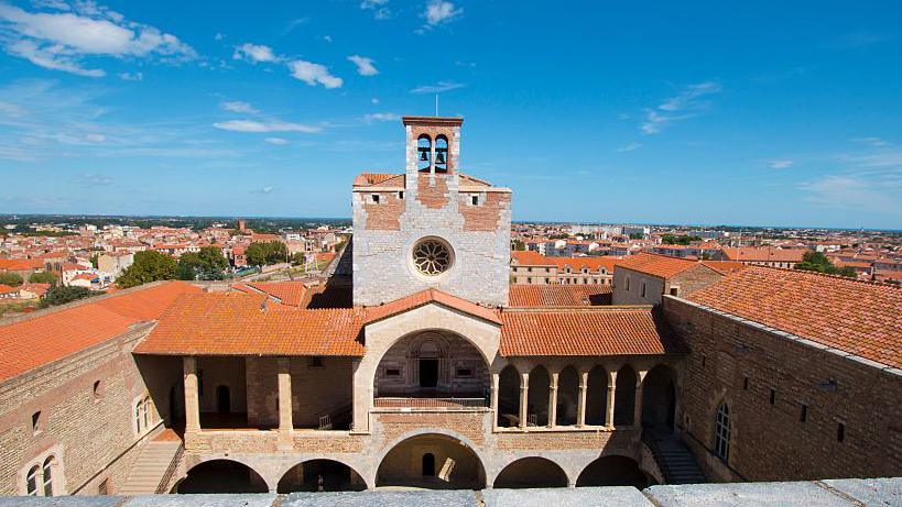General view of Perpignan, with a church clock tower overlooking the city against a blue sky.