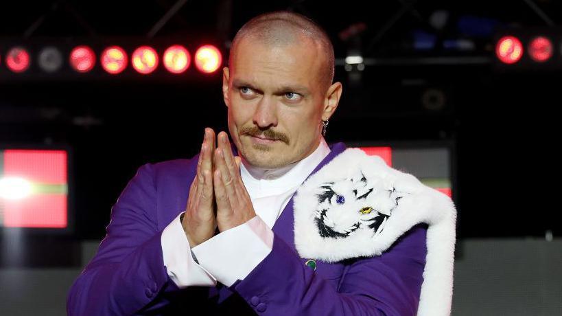 Oleksandr Usyk in a purple suit making a prayer sign with his hands