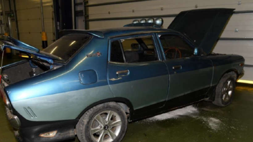 A blue, old-looking car with its bonnet and boot open in a dark warehouse