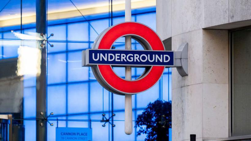 An image showing a blue and red roundel mounted on a metal pole at Cannon Street station, with blue-coloured glass visible behind it