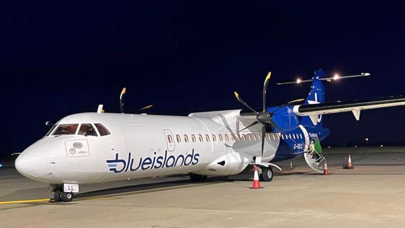 A Blue Islands plane on an airport runway in the night. It has a blue and white livery and is a propeller-powered plane