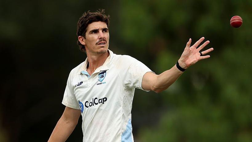 Sean Abbott extends his left arm to catch a red cricket ball, dressed in New South Wales' white kit