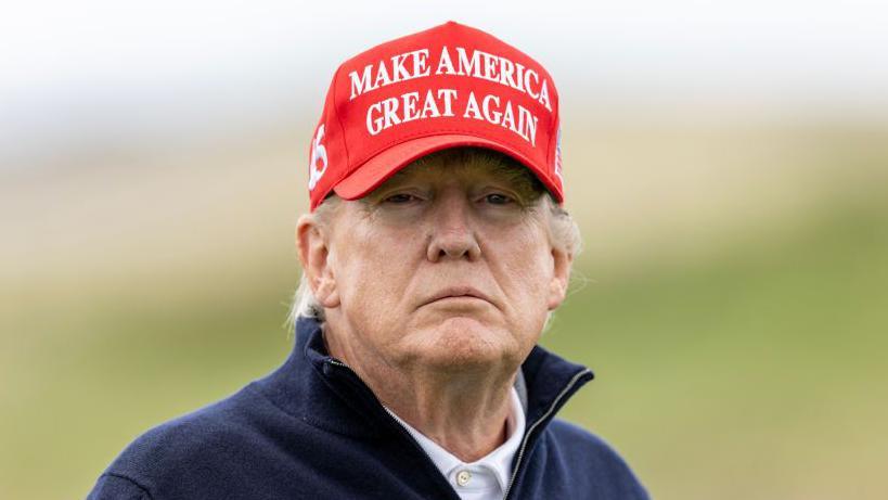 Donald Trump wearing a red cap with the words Make America Great Again on it