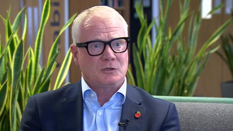 West Midlands mayor Richard Parker wearing glasses and a poppy. He is sitting on a sofa and there is a green plant behind him.  He has short white hair and wears a blue shirt and a darker blue jacket.