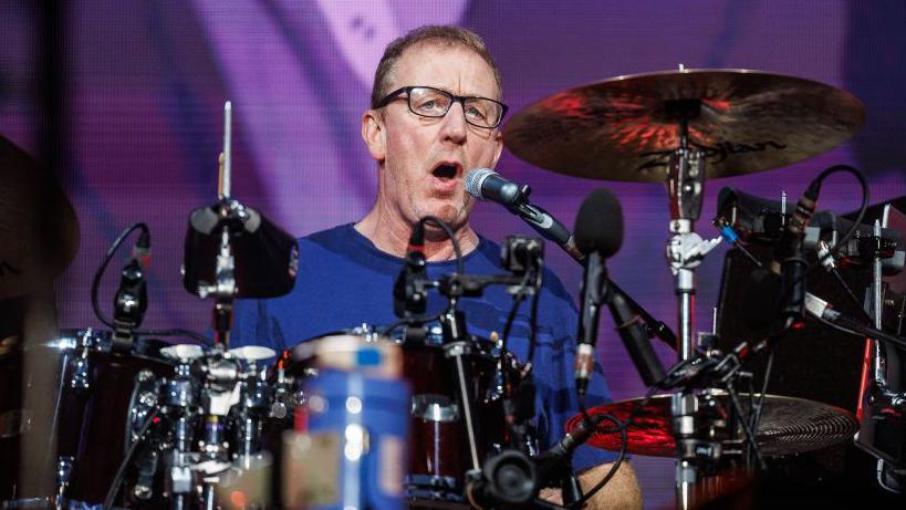 Dave Rowntree sitting at his drums singing into a microphone