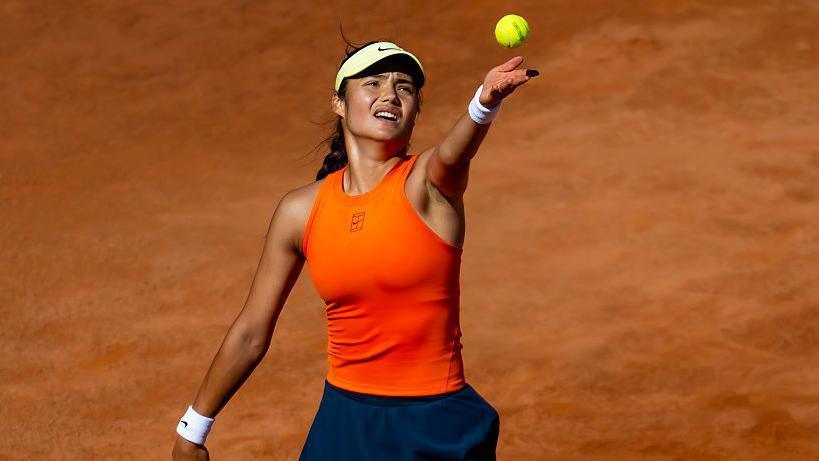 Emma Raducanu serves on a clay court