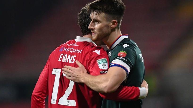 George Thomason of Bolton hugs Wrexham player George Evans after a game between the teams at the Racecourse