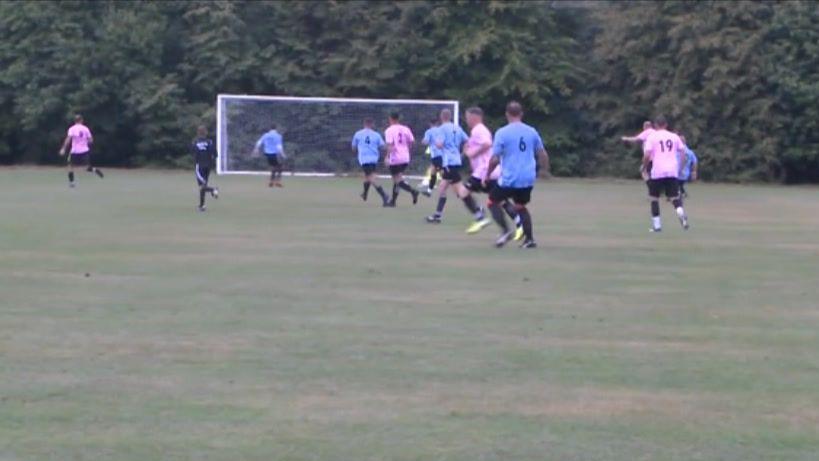 A football match with men on the pitch wearing pink shirts and blue shirts