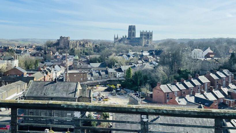 Durham Cathedral seen from a train travelling north and approaching Durham railway station. Houses can also be seen leading up to it.