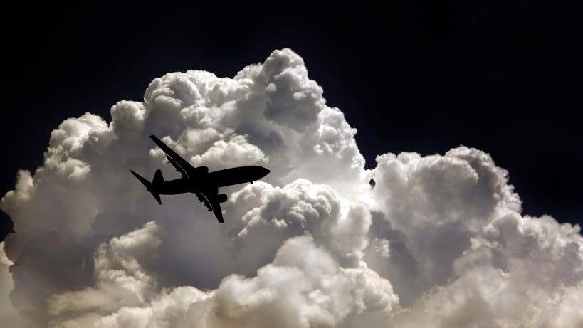 The silhouette of a plane against bright white clouds in a black sky