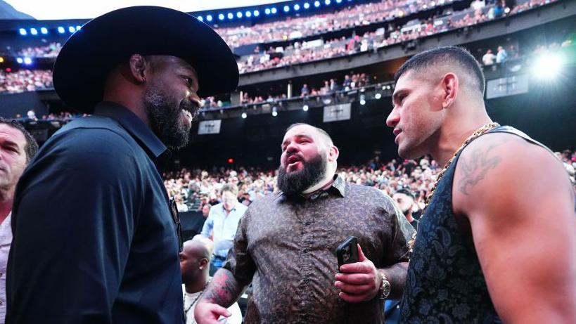 Jon Jones smiles in a cowboy hat speaking to fellow UFC fighter Alex Pereira at an event