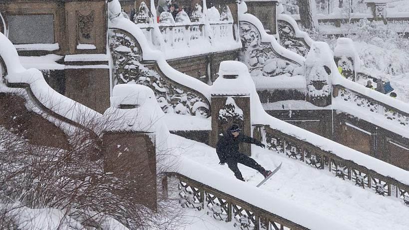 A person is snowboarding down some stairs covered in snow in Central Park, New York City. 
