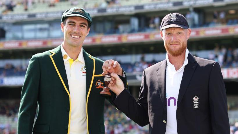 Pat Cummins and Ben Stokes holding the Ashes urn.