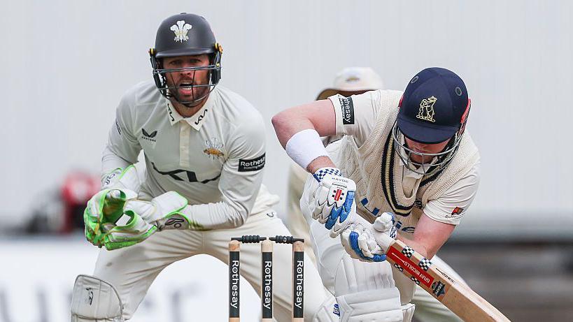 Left-handed Dan Mousley watchfully turns a ball to the legside as Surrey wicketkeeper Ben Foakes watches behind the stumps
