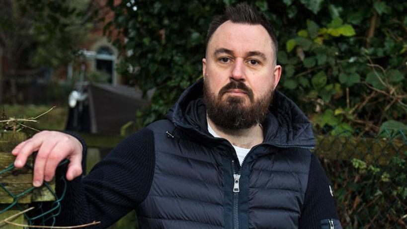 Martin Hibbert places a hand on a fence post as he poses for a photograph