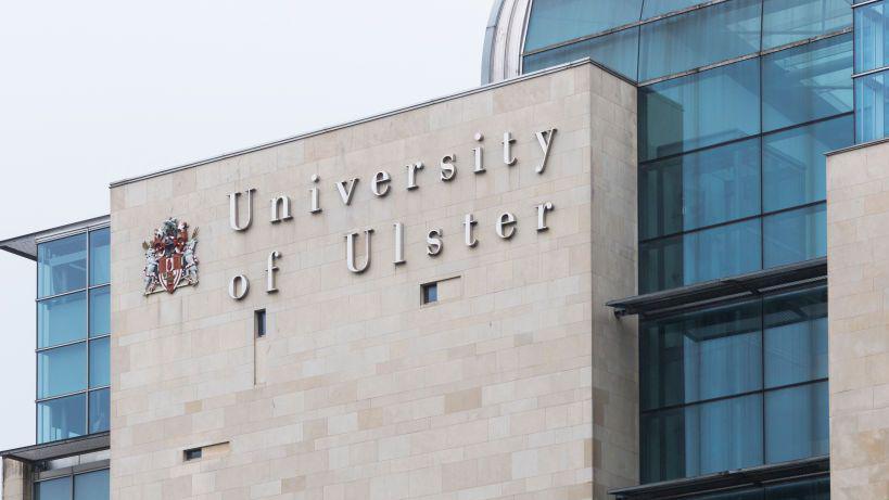 Ulster University Belfast in silver letters on the side of a grey bricked building.