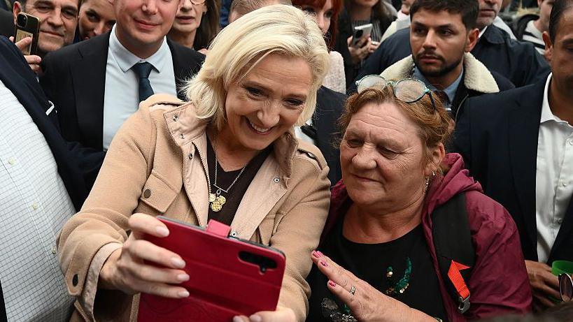 President of the parliamentary group of the French far-right Rassemblement National (RN) party Marine Le Pen (C) poses for a selfie photograph with a supporter at a livestock show