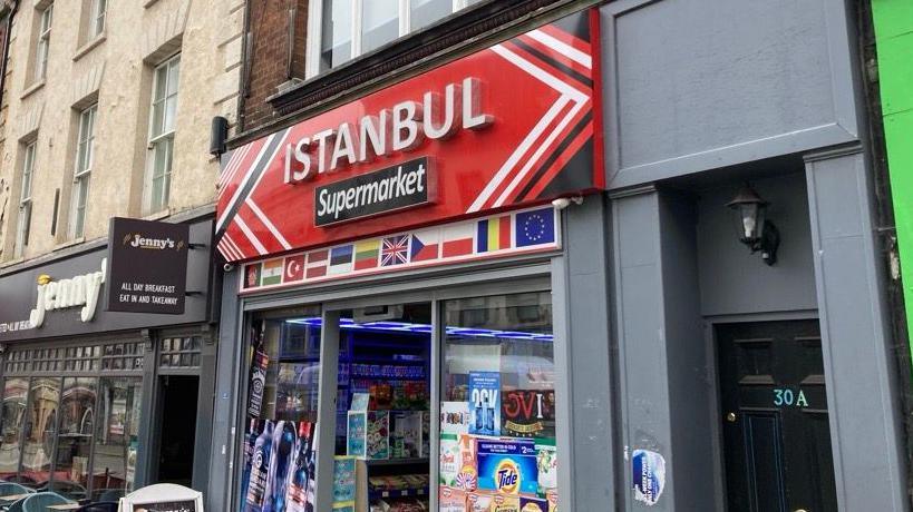 The front of the Istanbul Mega Market convenience store. The sign of the shop is red and it says in white writing ISTANBUL Supermarket.